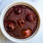 Rich cherry chocolate microwave mug cake in a white ramekin, showcasing a moist, decadent dessert topped with fresh cherries, perfect for quick healthy dessert recipes.