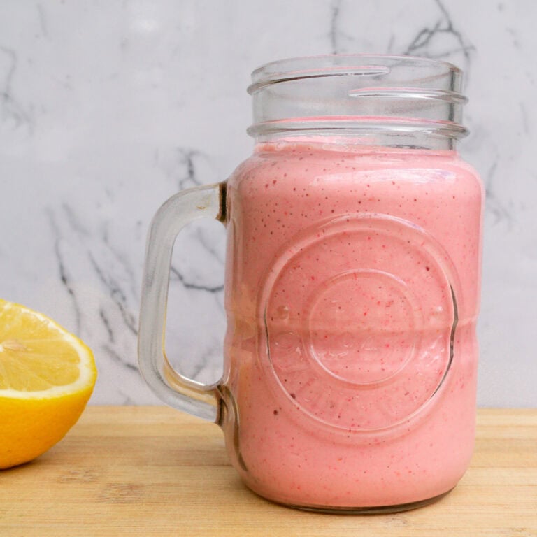 Fresh strawberry lemon smoothie in a mason jar with a lemon wedge on a wooden surface, perfect for healthy eating, fruit smoothies, and summer beverages.