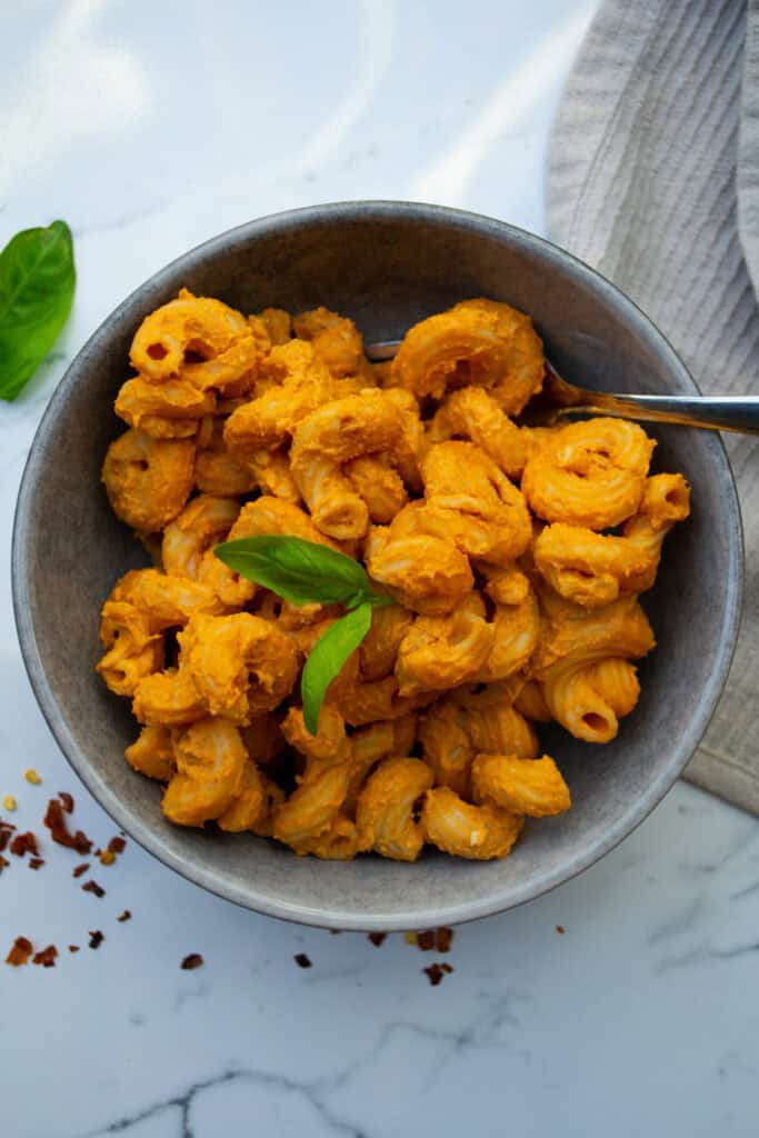 Creamy vegan macaroni and cheese with a rich, cheesy sauce, garnished with fresh basil in a gray bowl. Perfect comfort food recipe, easy to make, and full of flavor for plant-based diets.