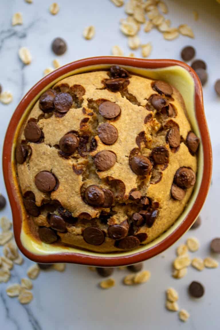 Creamy chocolate chip cookie skillet in a rustic ceramic dish with scattered oats and chocolate chips around it, perfect for a delicious homemade dessert.