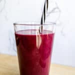 Fresh berry smoothie in a tall glass with a black-and-white striped straw, on a wooden surface, highlighting healthy, vibrant, and nutritious breakfast options.