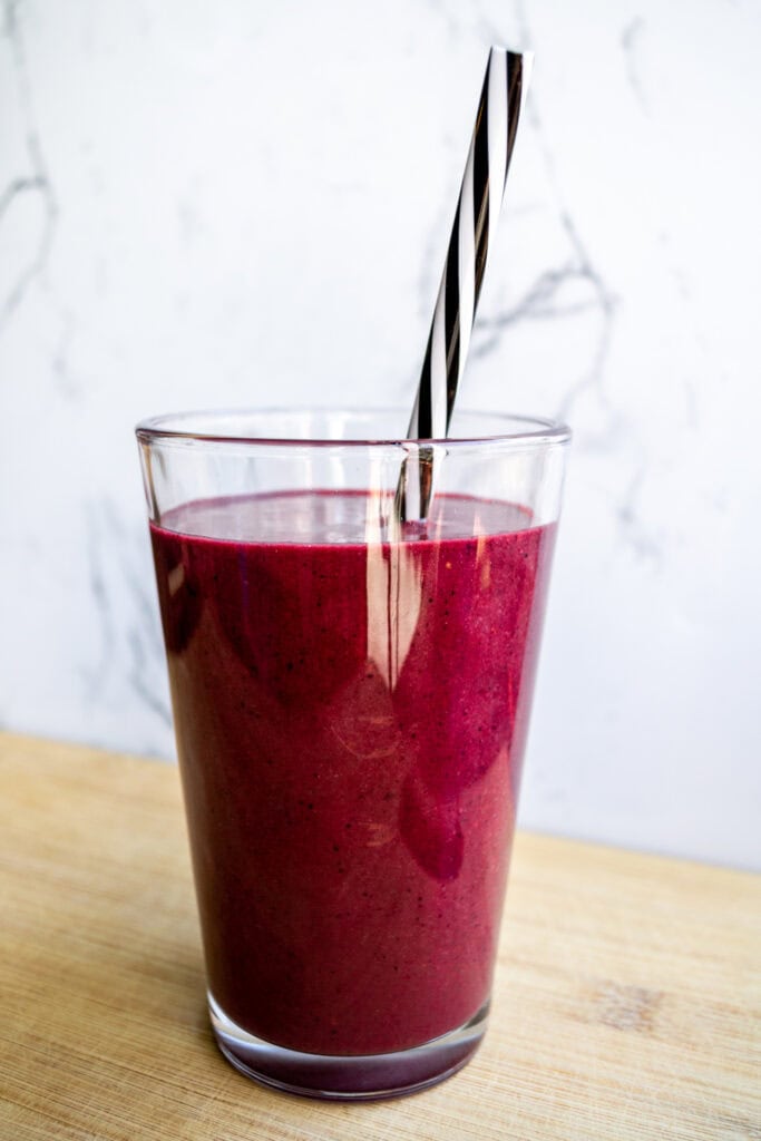 Fresh berry smoothie in a tall glass with a black-and-white striped straw, on a wooden surface, highlighting healthy, vibrant, and nutritious breakfast options.
