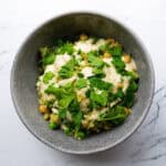 Creamy vegetable salad with peas, chickpeas, and fresh parsley in a gray bowl on a white marble surface.