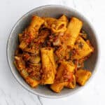 Creamy vegetable pasta in a gray bowl, topped with rich tomato sauce, cooked with zucchini, mushrooms, and onions, served on a white marble surface.