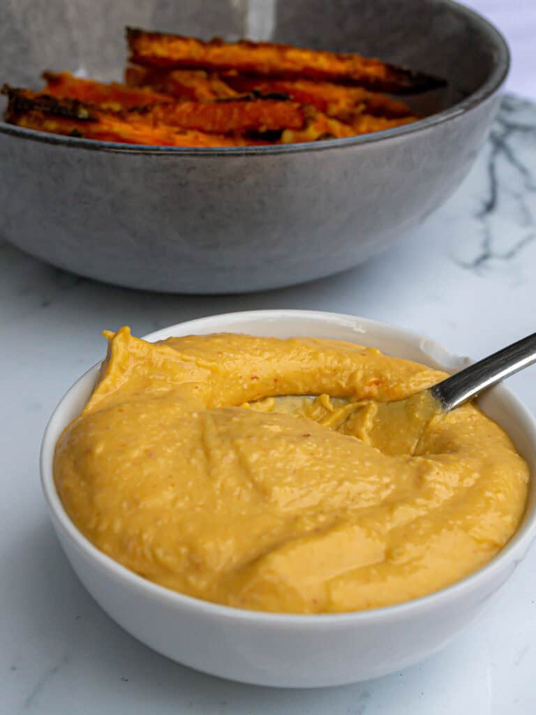 Creamy homemade cheese dip served in a white bowl with a spoon, featuring melted cheese and a smooth texture, perfect for snacking or appetizers.