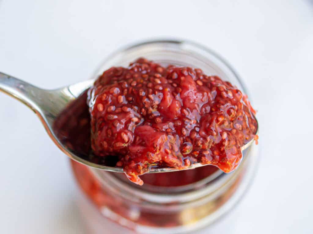 Fresh homemade strawberry jam in a glass jar with a metal spoon, highlighting natural fruit preserves.