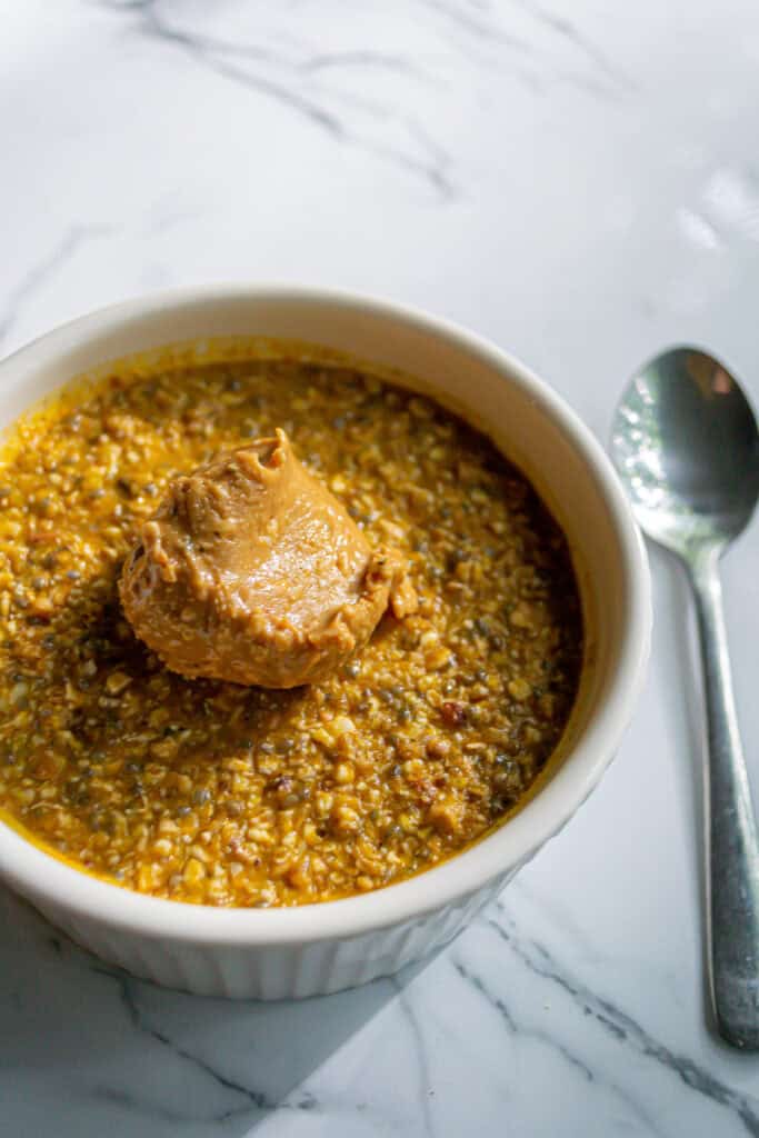 Savory peanut butter chicken stew in a white ramekin with a spoon on a marble surface.