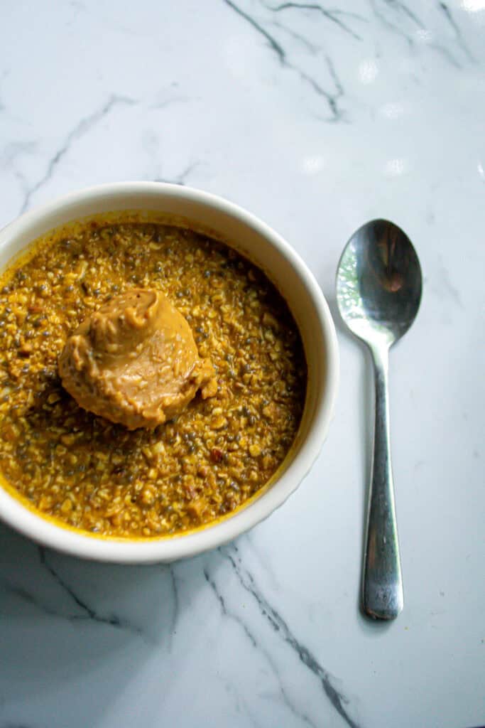 Creamy lentil soup with a dollop of peanut butter on top, served in a white bowl on a marble surface with a silver spoon. Perfect for healthy, hearty meals and packed with plant-based protein.
