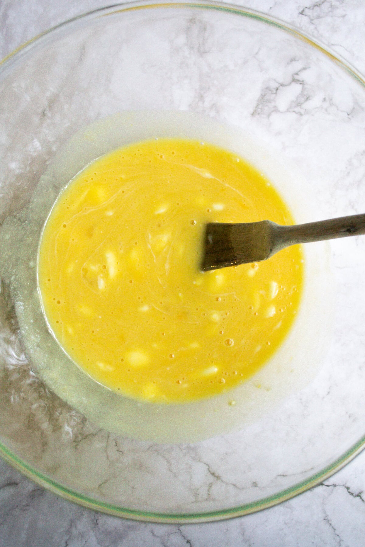 Creamy yellow beaten eggs in a glass mixing bowl, ready for cooking or baking.