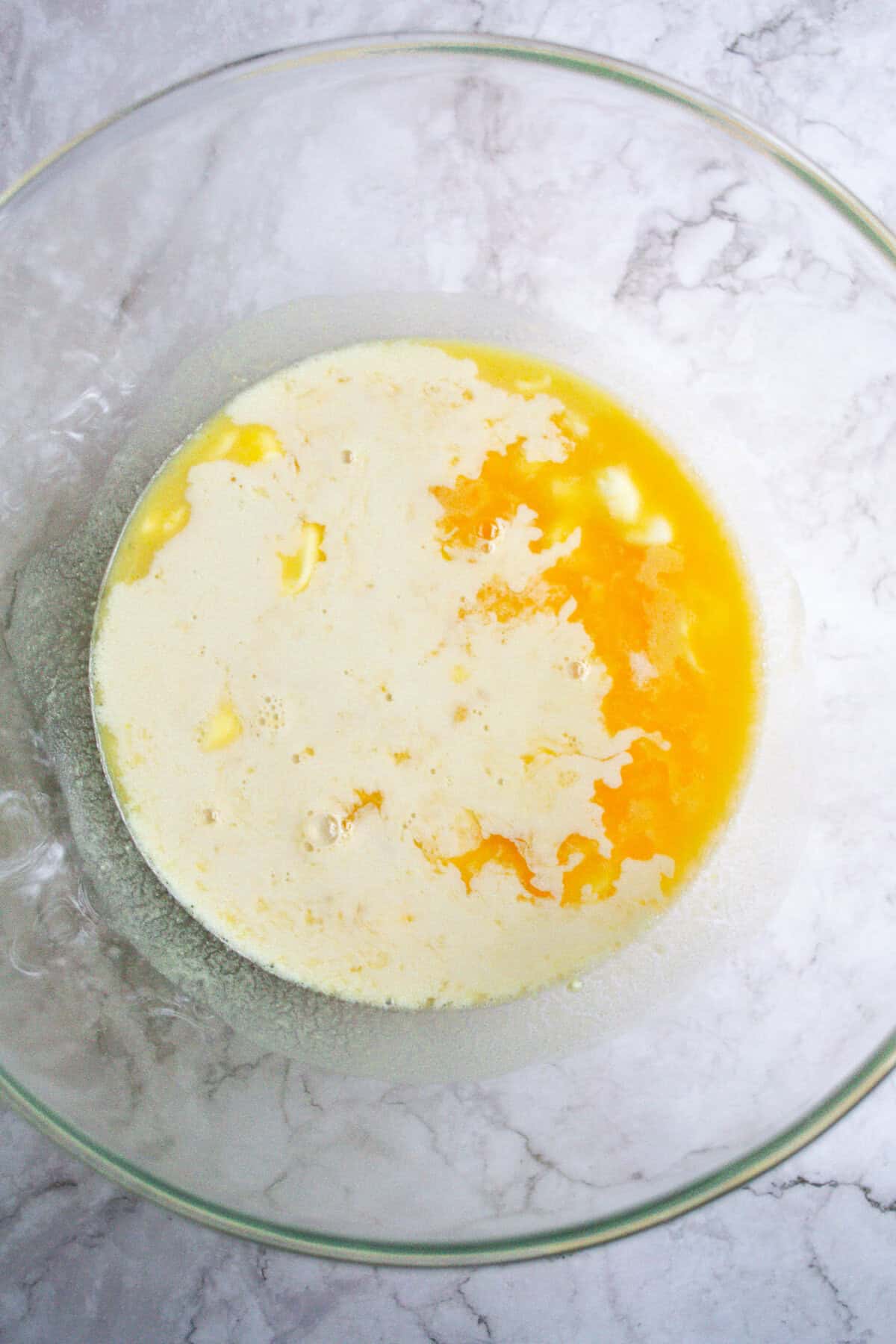Creamy beaten eggs in a glass mixing bowl, ready for cooking or baking, on a marble surface.