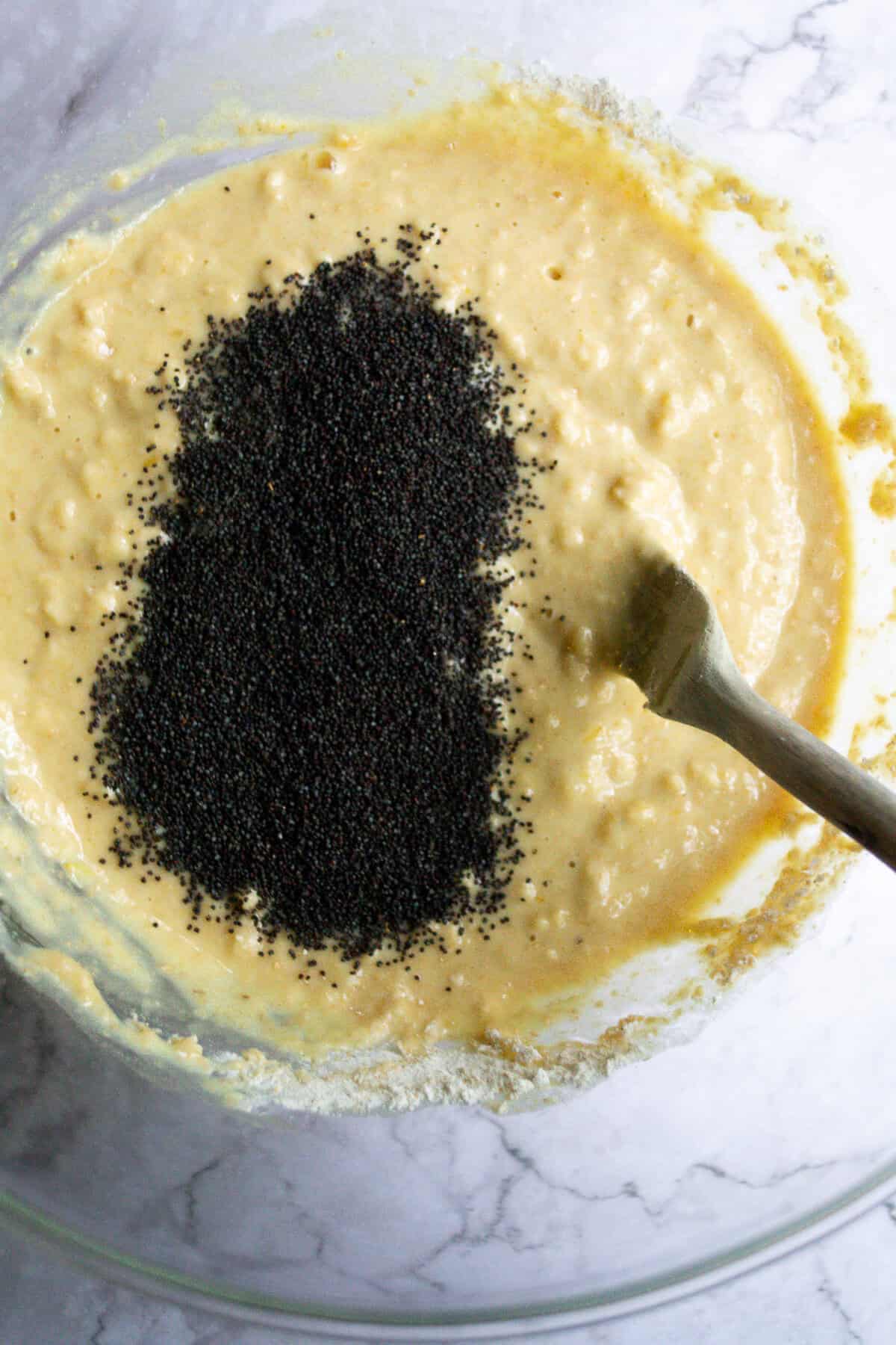 Black poppy seeds in a batter mixture, ready to be mixed for baking or cooking.