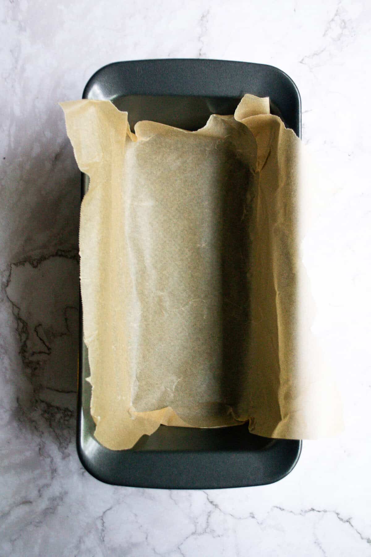 Unlined metal loaf pan with parchment paper ready for baking bread or cakes, ideal for homemade baking recipes, kitchen essentials, and baking tips.