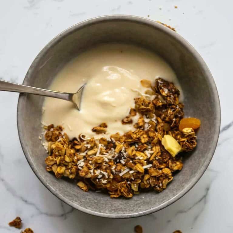 Butternut squash granola with yogurt and dried fruit in a metallic bowl on a white marble surface.