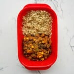 Sweet potato and black bean chili with rice meal prep in a red container, healthy vegetarian dinner, plant-based protein source, easy meal for lunch or dinner, gluten-free and vegan friendly.