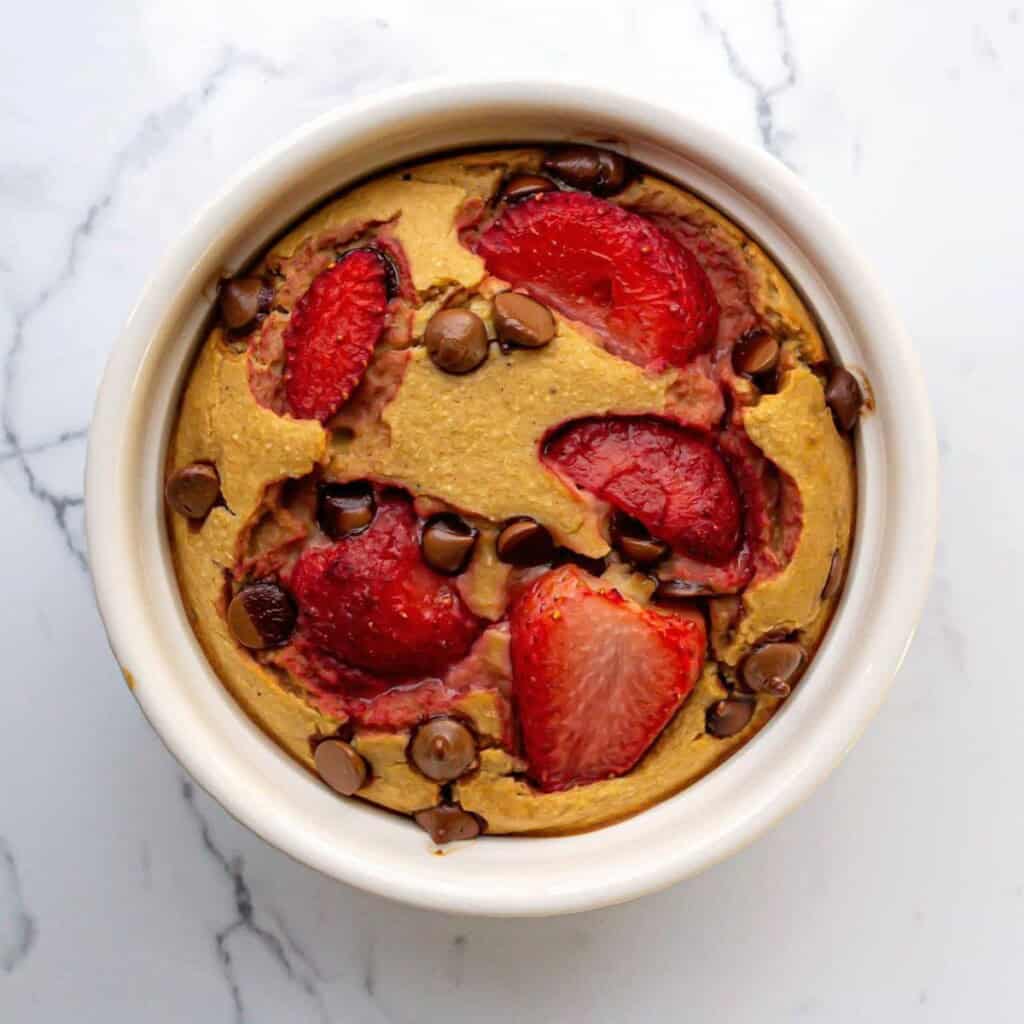 Fresh strawberry and chocolate chip baked dessert in a white ramekin, featuring a golden-brown crust and vibrant red fruit pieces. Perfect for healthy, delicious treats or breakfast options.