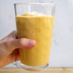 Creamy mango smoothie in a tall glass with a hand holding it, showcasing fresh, healthy, easy smoothies for breakfast and snacks.