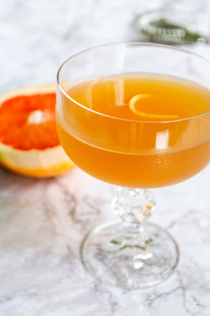 Grapefruit daiquiri in a crystal glass on a white marble table with a grapefruit in the background.