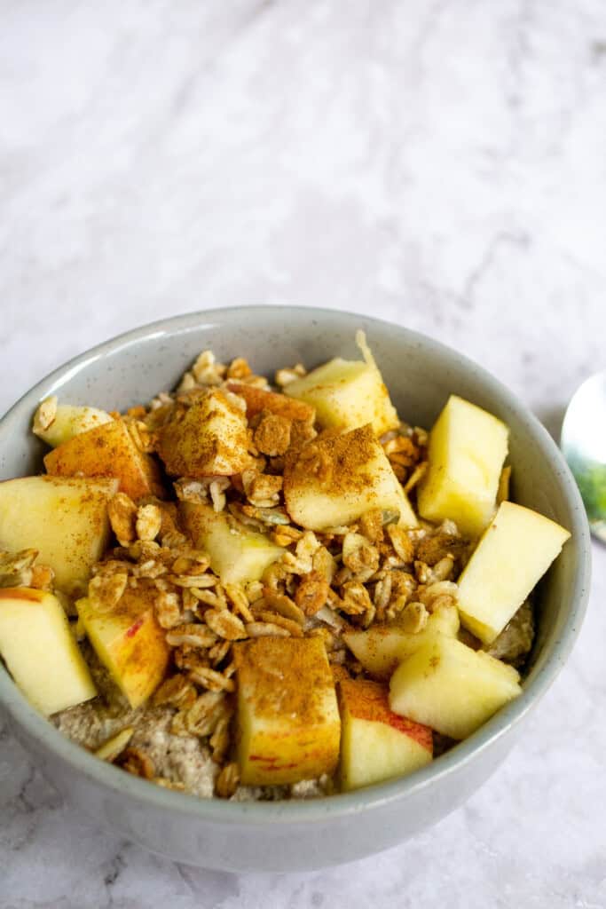 Fresh apple chunks with granola and cinnamon in a light grey bowl, healthy breakfast or snack option.