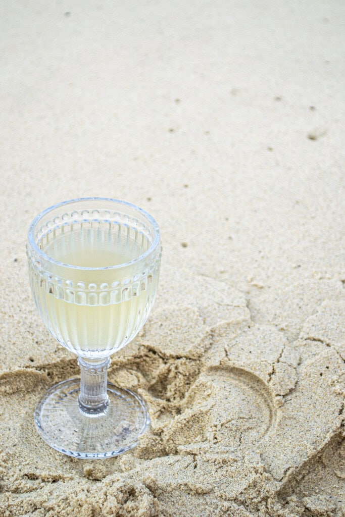 Fresh homemade lemonade served in an elegant glass on sandy beach, perfect for summer refreshment and tropical vacation drinks.