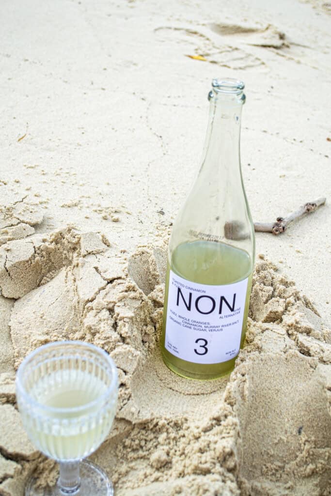 Refreshing non-alcoholic beverage bottle on sandy beach, perfect for summer drinks and beachside relaxation, featuring unique label design and light green liquid.