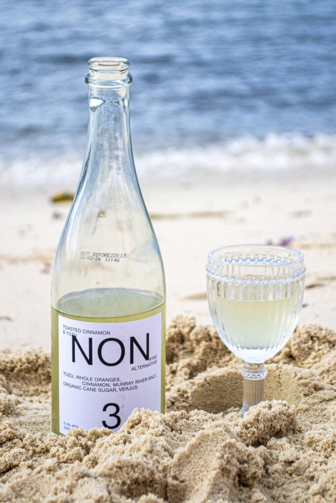 Refreshing non-alcoholic beverage bottle with a glass on a sandy beach, promoting healthy lifestyle and alternative drinks, perfect for beach days and summer relaxation.