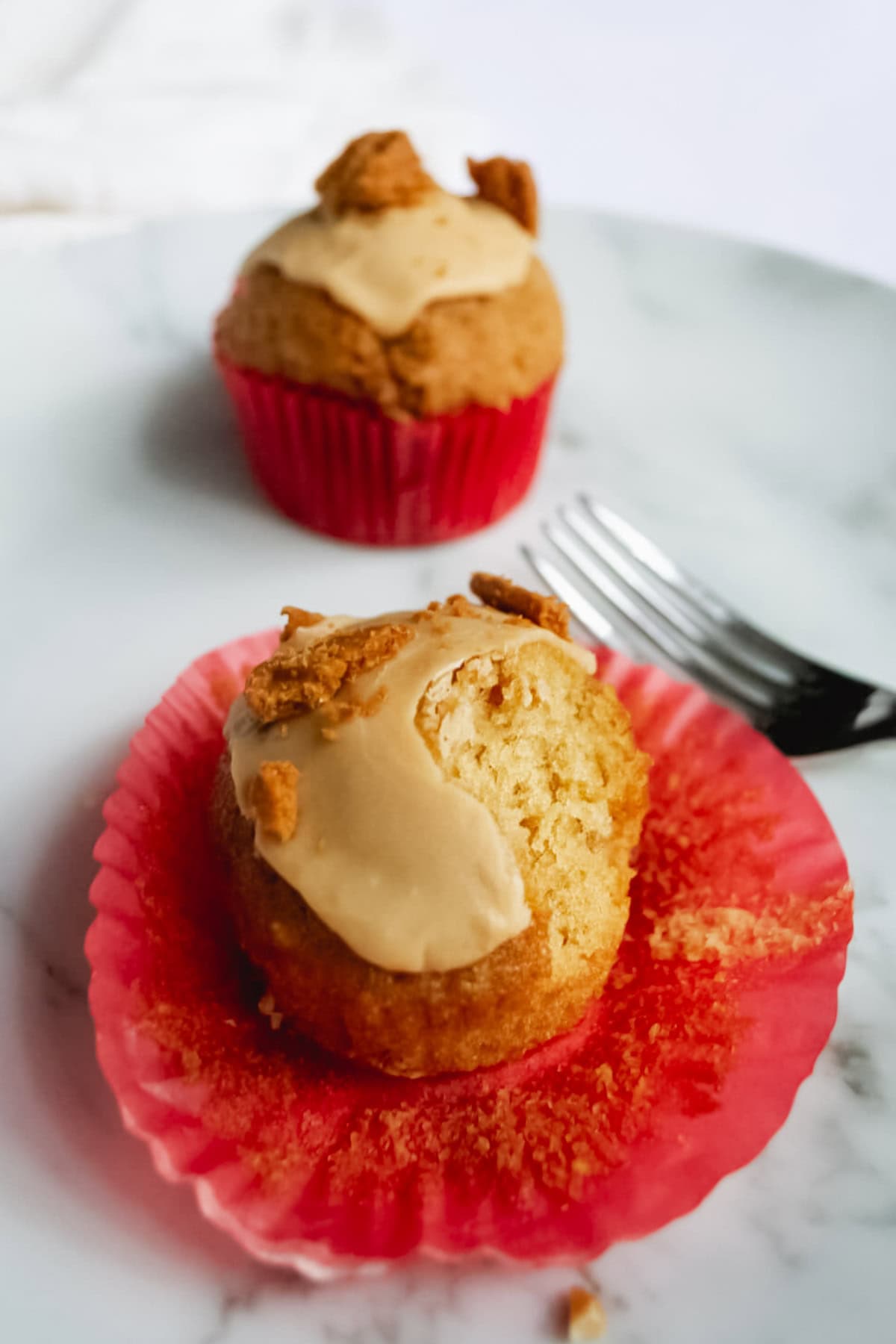 Homemade vanilla bean cupcake with crumb topping on pink cupcake liner, served on marble surface with fork.