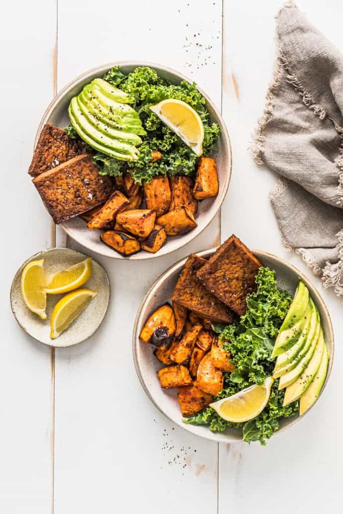 Overhead view of two sweet potato tofu nourish bowls on a white wooden table.