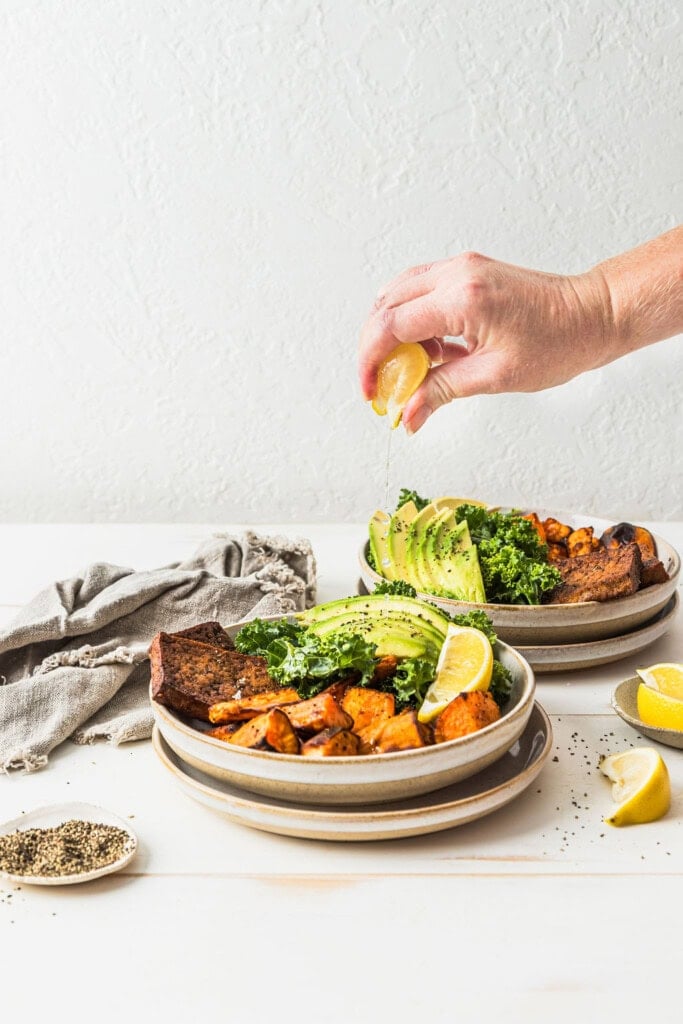 Front view of a hand squeezing even more lemon juice over the top of a sweet potato tofu nourish bowl.
