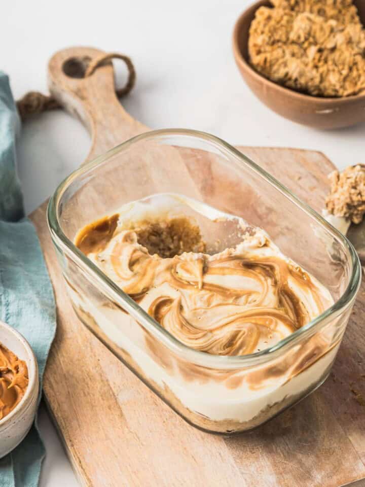 Creamy peanut butter and honey swirl ice cream in a glass baking dish with peanut butter, honey, and vanilla ingredients on a wooden cutting board.