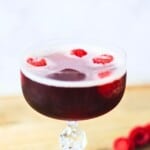 Sweet red wine spritzer garnished with fresh raspberries in a glass on a light background.