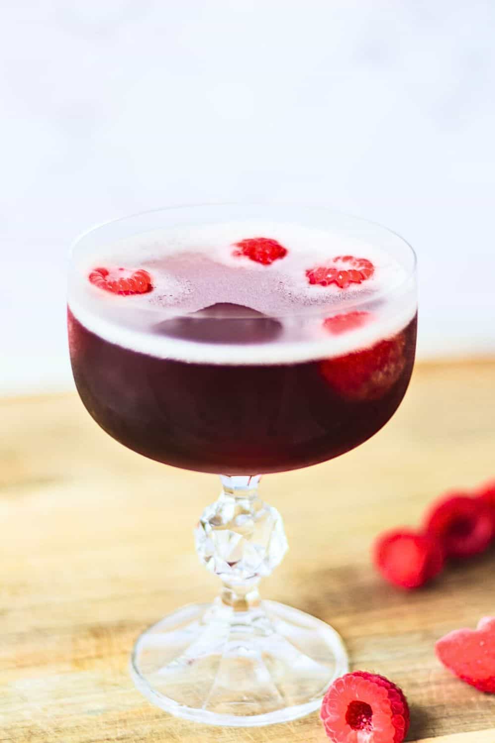 Fresh raspberry wine cocktail in a decorative glass with floating raspberries and foam, perfect for summer drinks.