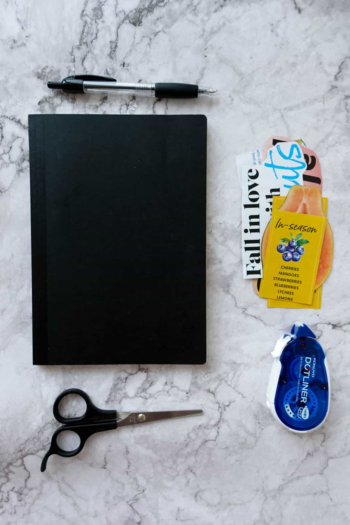 Overhead shot of a new cooking journal, with magazine cutouts, dot liner, pen and scissors surrounding it.