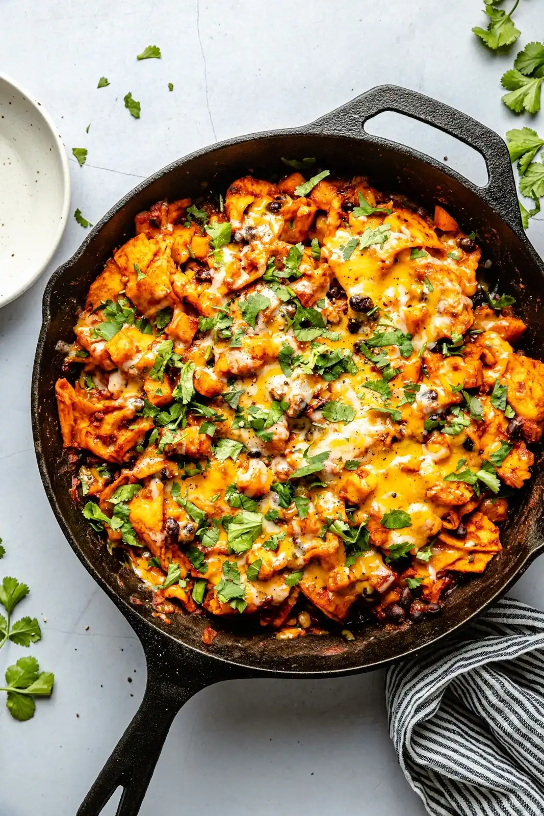 Overhead view of black bean enchilada skillet in a cast-iron pan on white table.