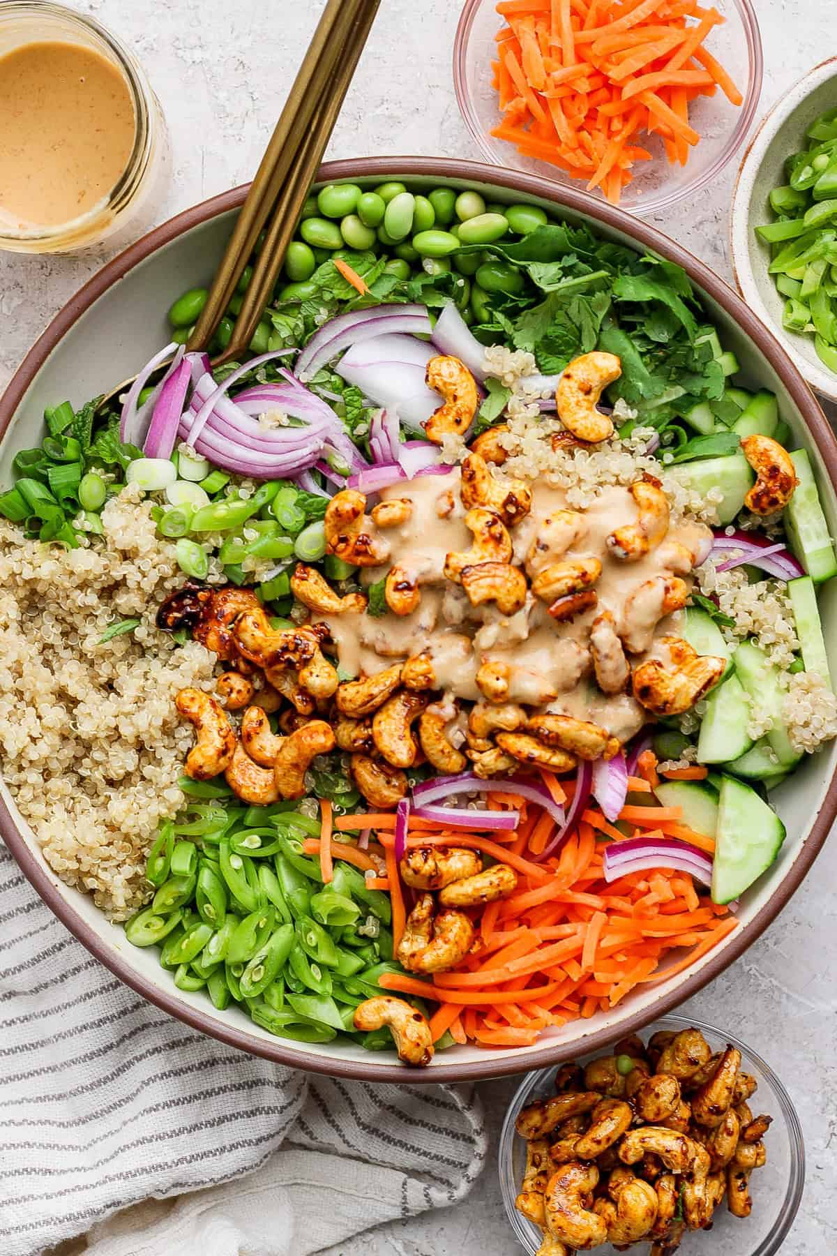 Fresh veggie Buddha bowl with quinoa, shredded carrots, cucumbers, green onions, avocado, red onion, cilantro, and toasted cashews with a creamy dressing on top.
