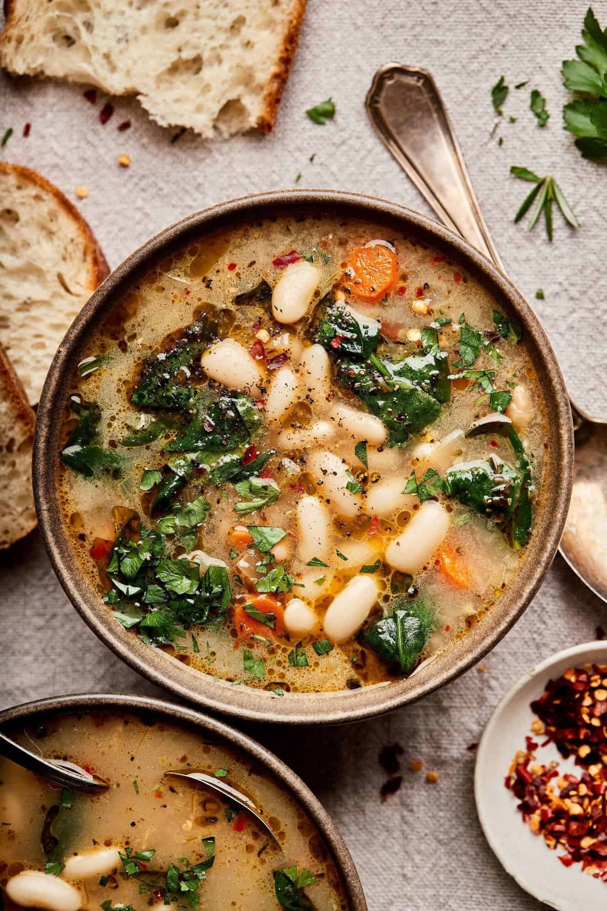Creamy white bean vegetable soup garnished with fresh herbs, served in a rustic bowl with slices of crusty bread; healthy and hearty vegetarian meal perfect for cozy nights.