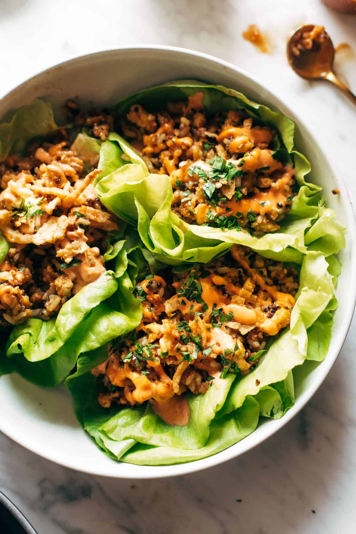 Crispy lettuce wraps with seasoned ground chicken, vegetables, and spicy sauce in a white bowl, healthy Asian-inspired appetizer or lunch.