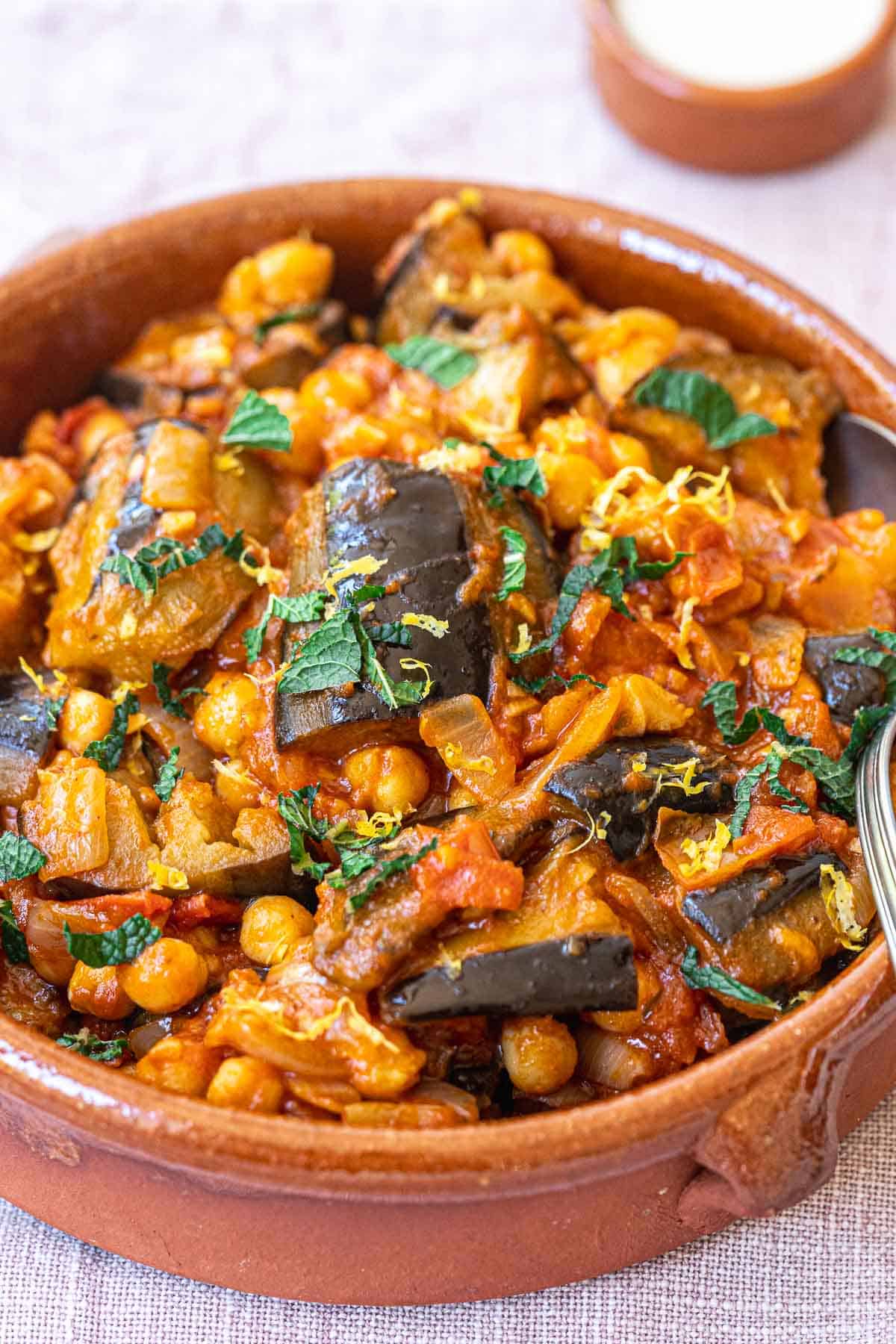 Braised vegetable stew with eggplant, chickpeas, and herbs in a rustic clay bowl, showcasing healthy and flavorful vegetarian meal options.