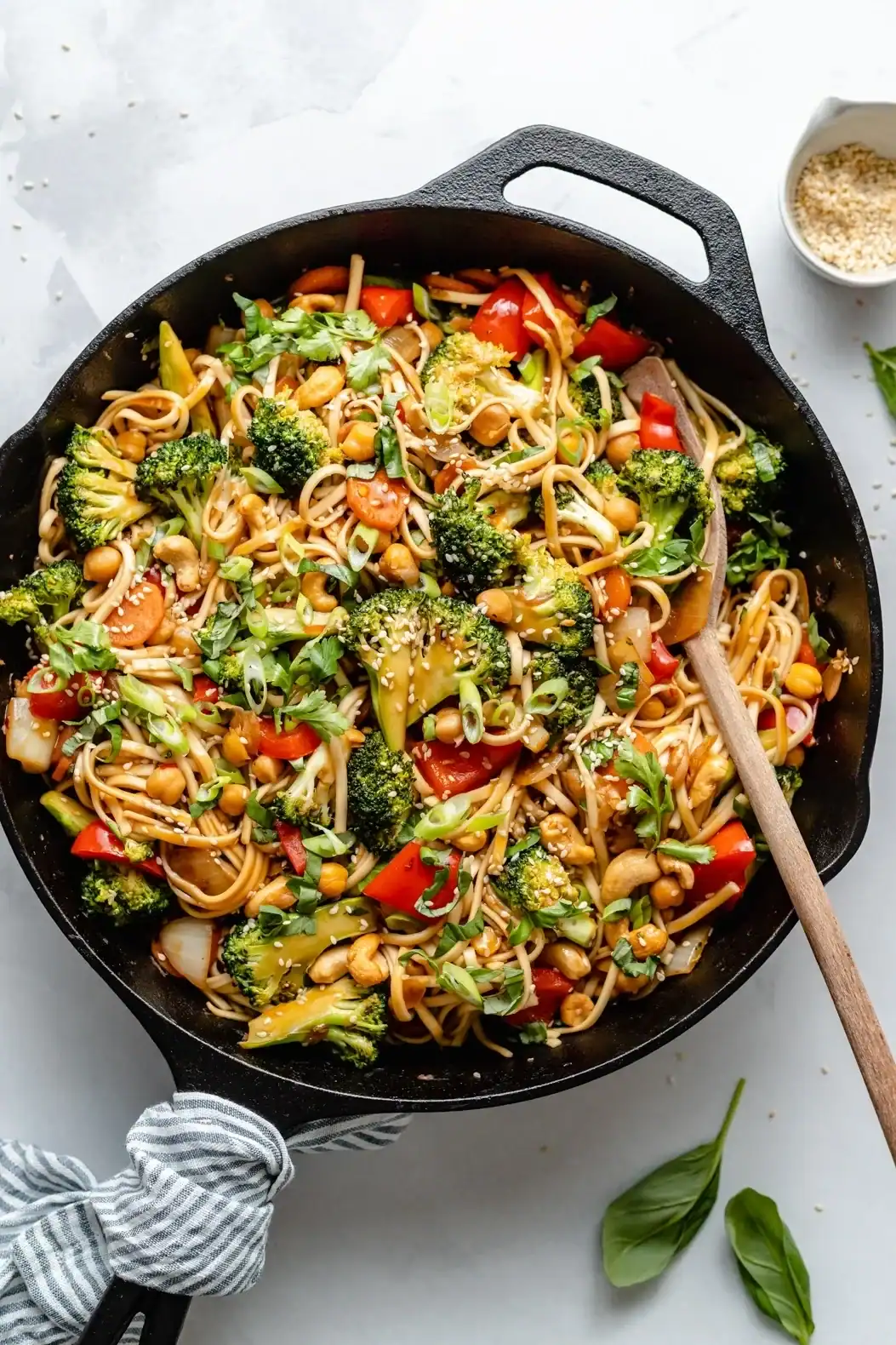 Overhead view of a veggie noodle stir fry in a cast iron pan on a white table.