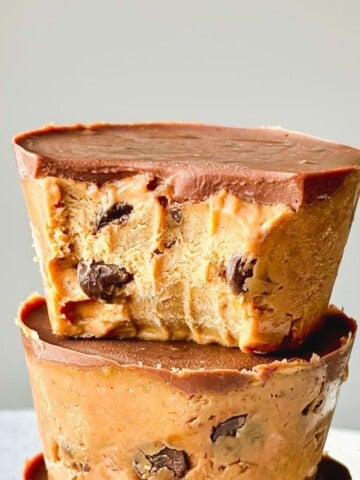 A cookie dough cup sitting on top of another cookie dough cup against a light grey background.