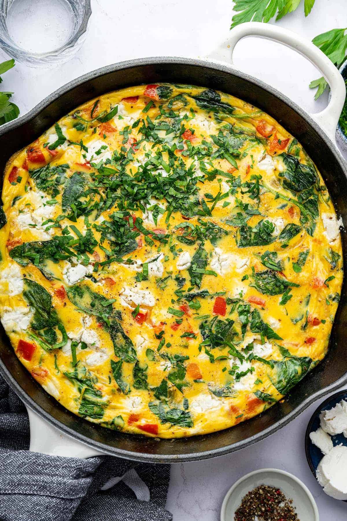 Savory vegetable and cheese frittata in a skillet, featuring fresh herbs, spinach, red peppers, and eggs, perfect for breakfast or brunch.