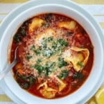 Overhead shot of vegetarian tortellini soup topped with parmesan and coriander in a white bowl.