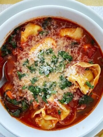 Overhead shot of vegetarian tortellini soup topped with parmesan and coriander in a white bowl.