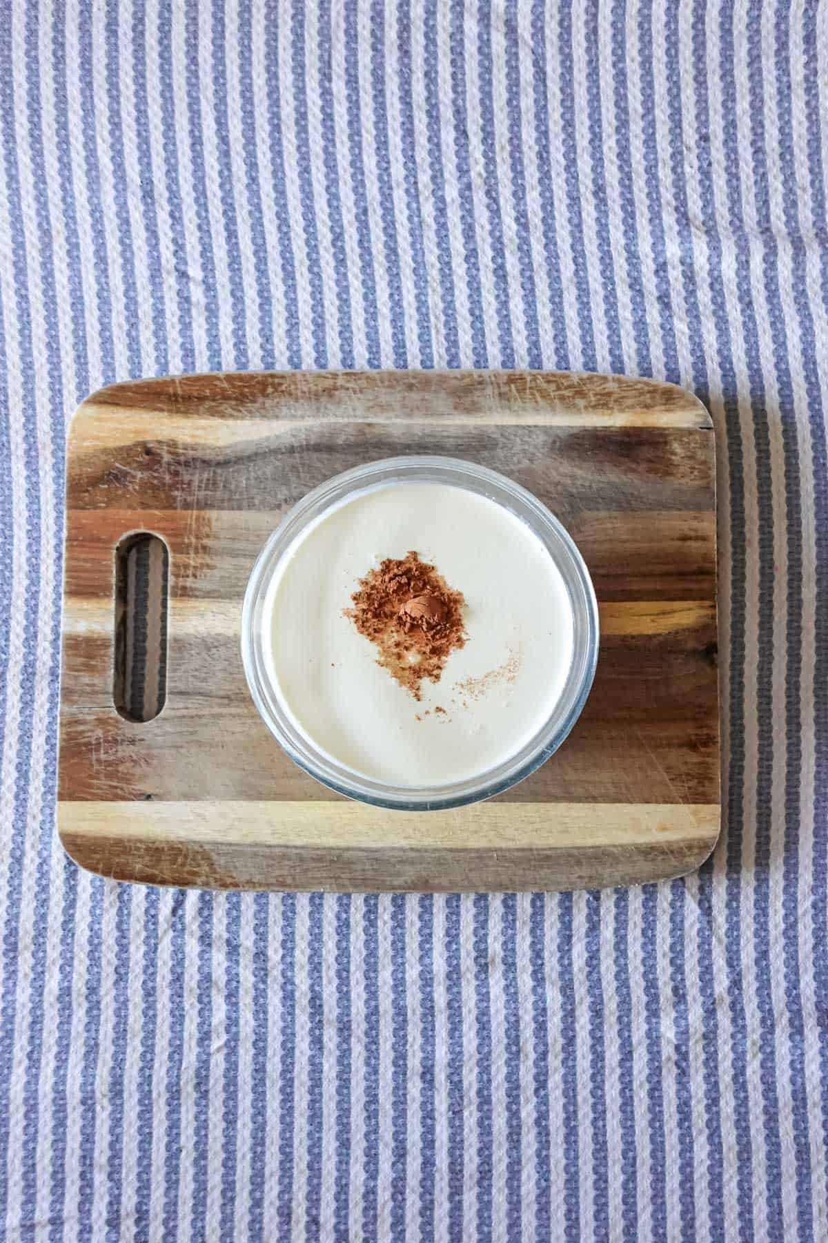 Creamy vanilla pudding topped with a sprinkle of cinnamon on a wooden cutting board, served with a cozy striped fabric background. Perfect for a homemade dessert or snack.
