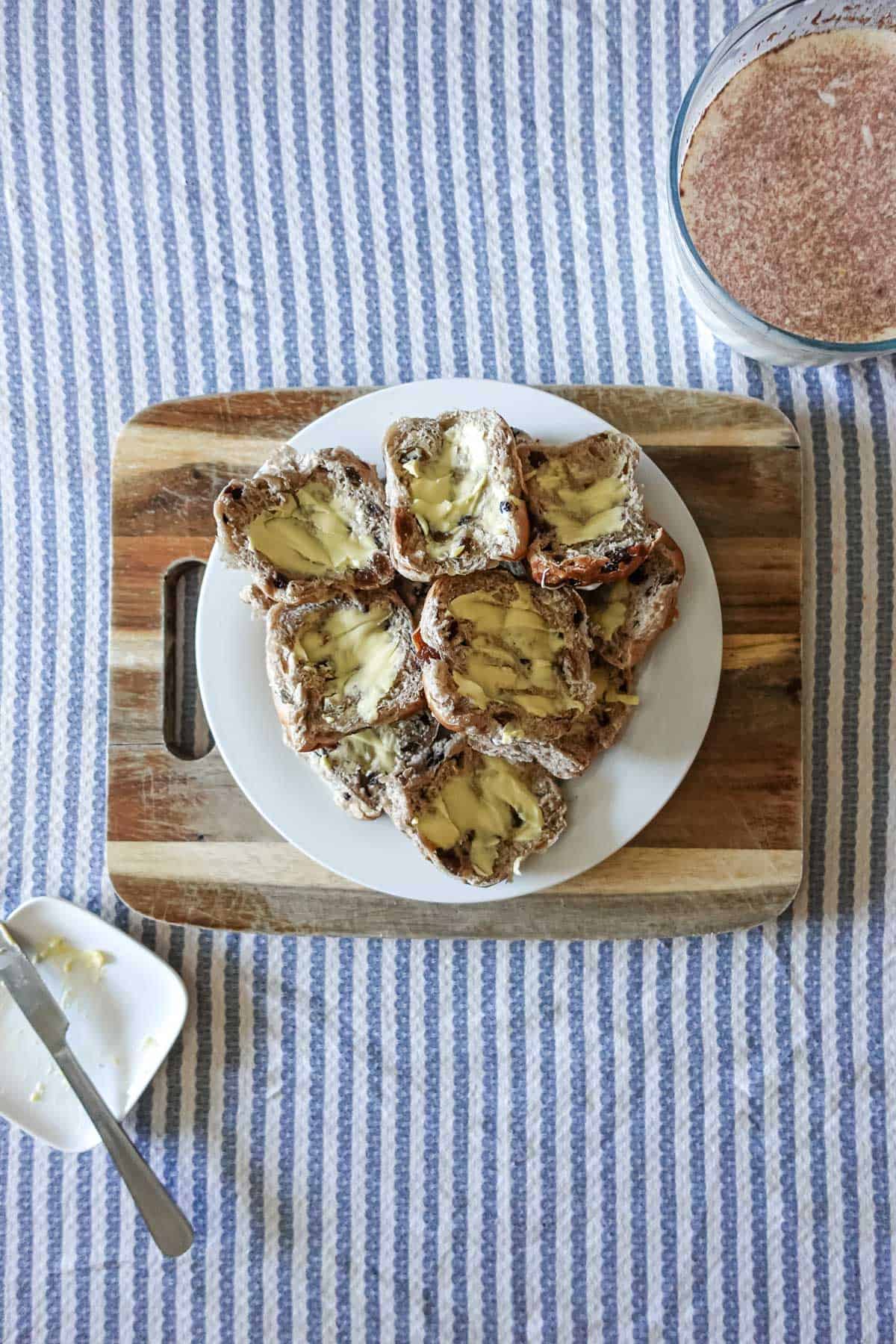 Buttery cinnamon raisin toast with melted butter on a white plate, served on a rustic wooden tray with a blue striped tablecloth, promoting fresh homemade breakfast ideas and wholesome food recipes.