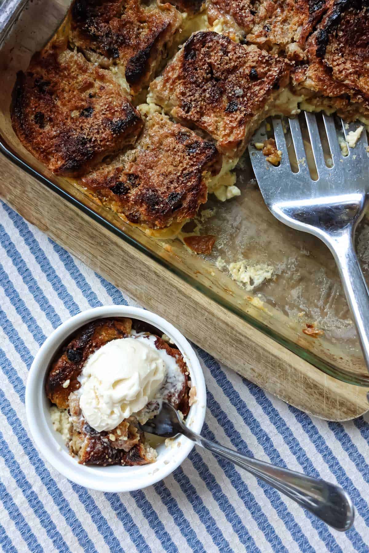 Golden-brown baked bread pudding with caramelized topping and vanilla ice cream, served with a slice in a small bowl, perfect for dessert.