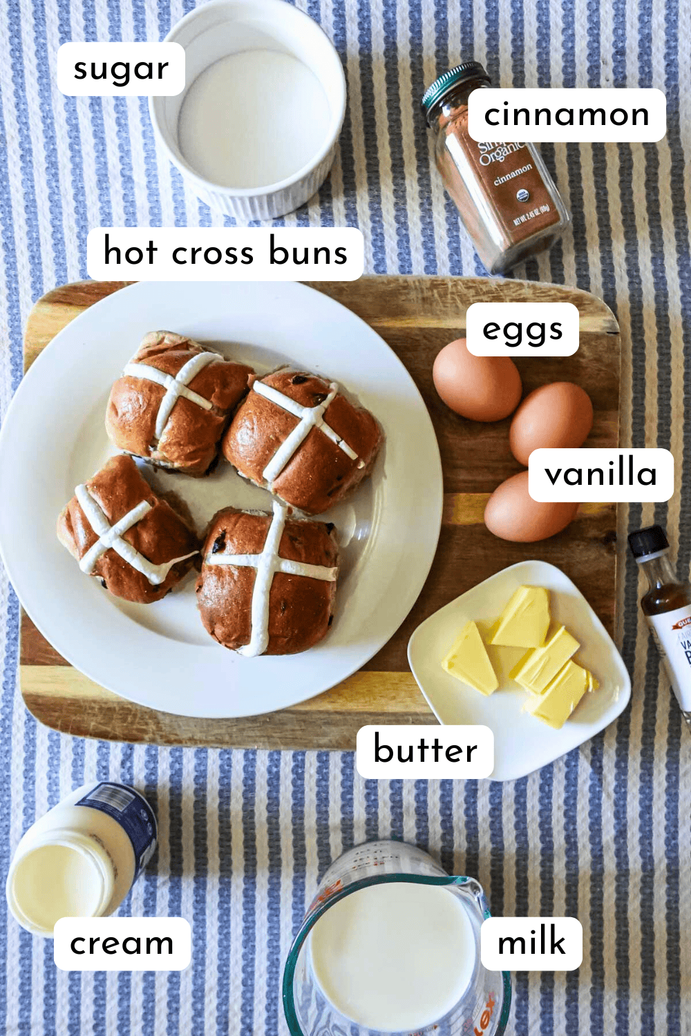 Sweet cinnamon bread rolls with vanilla icing, surrounded by eggs, butter, cream, milk, sugar, and cinnamon spice on a wooden cutting board, perfect for homemade breakfast or brunch recipes.