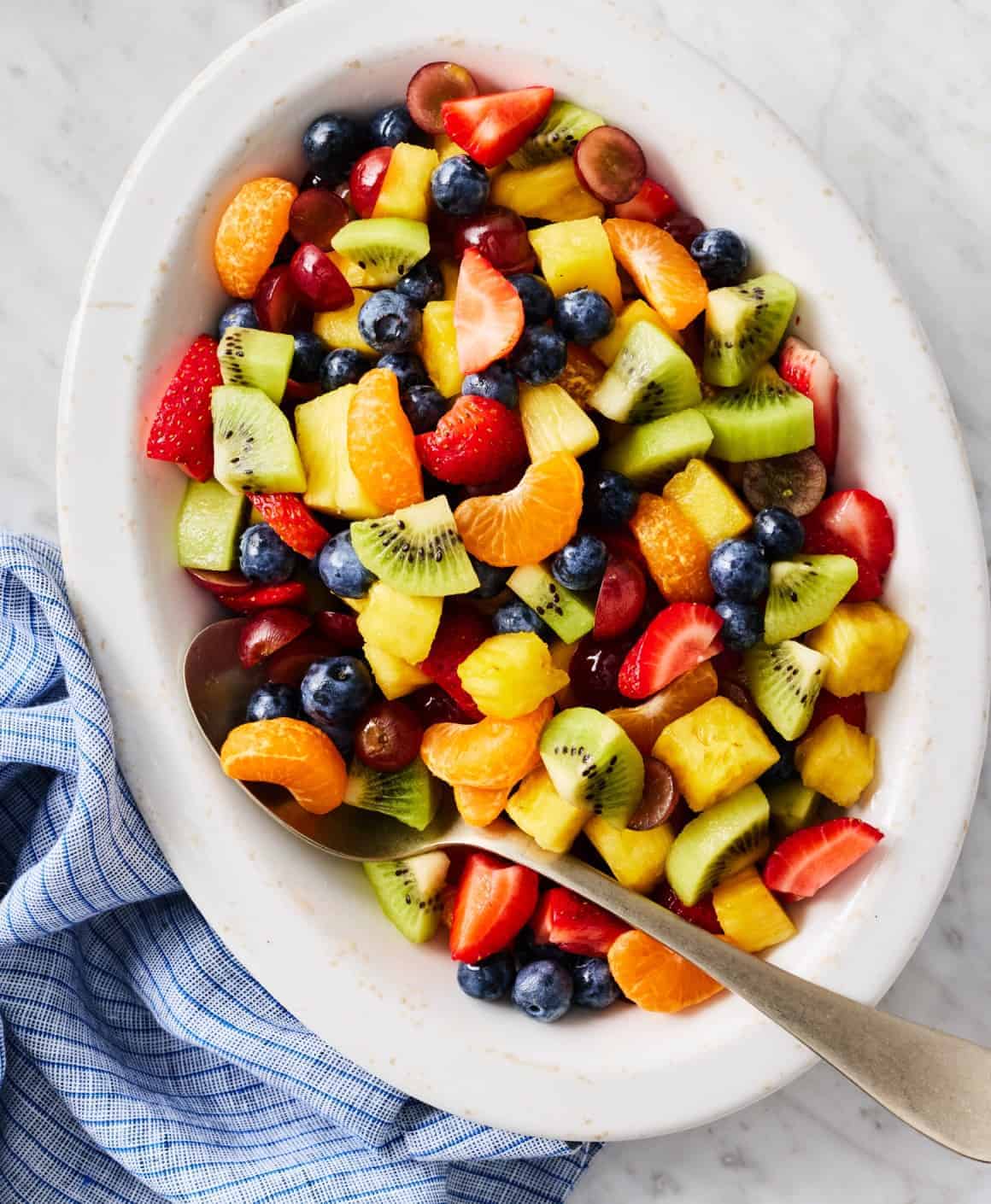 Fresh fruit salad with mixed berries, pineapple, kiwi, and orange slices in a white serving dish.