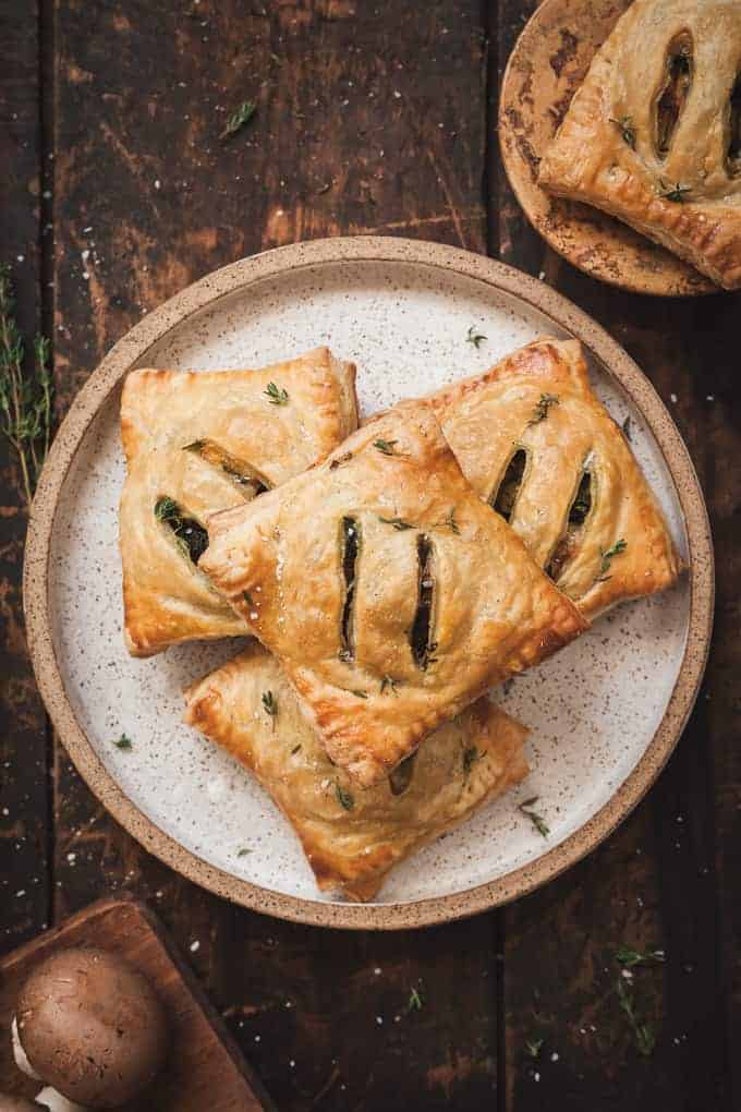 Overhead view of golden, flaky savoury hand pies on a white plate, sprinkled with dried herbs.