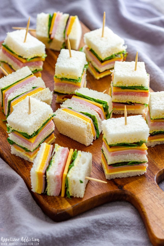 Mini ham and cheese sandwiches on a wooden board, perfect for parties or snacks.