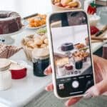 iPhone photographing fresh homemade desserts with fruit, chocolate, and baked goods for a cosy gathering.